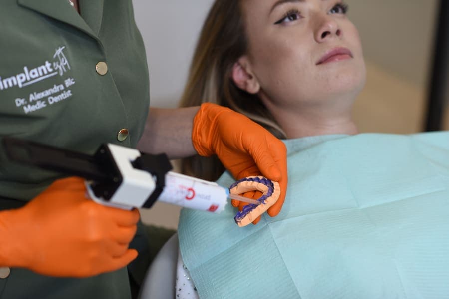 Medic pregătind cheia de silicon cu lucrarea provizorie, deasupra unei paciente în unitul dentar