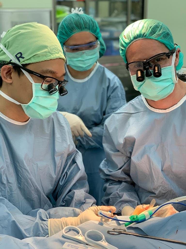 Trei chirurgi cu lupe chirurgicale și câmpuri sterile, în timpul unei intervenții oro-maxilo-faciale